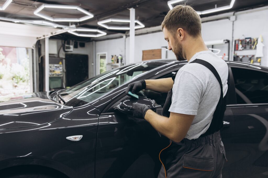 Professional Auto Mechanic Applying Protective Film to Car Mirror in Workshop